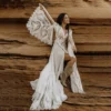Bride posing beside sandstone rocks in flowing boho lace bridal gown
