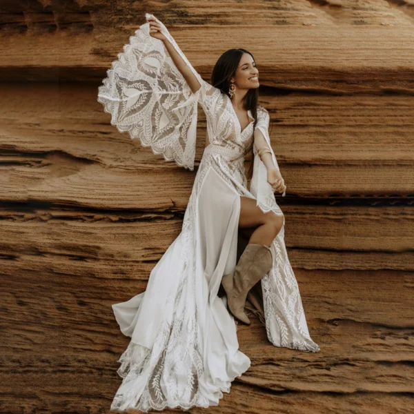 Bride posing beside sandstone rocks in flowing boho lace bridal gown