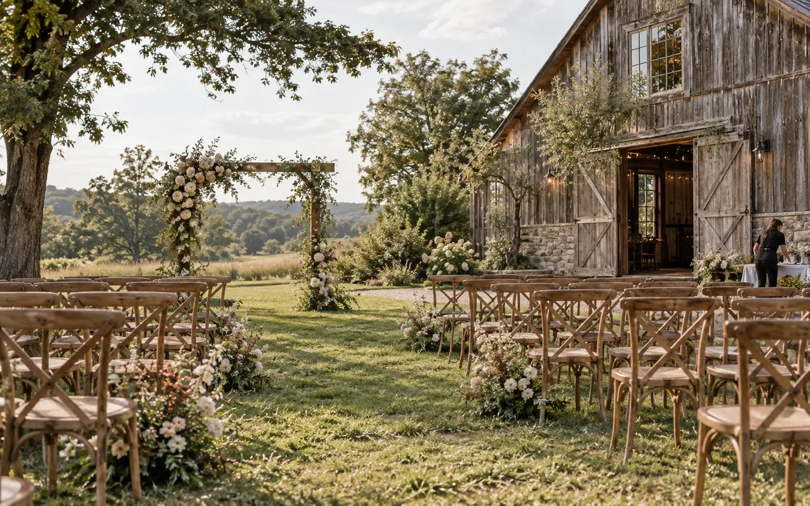 Outdoor rustic barn wedding ceremony with wooden chairs and a floral arch